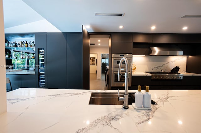 kitchen featuring stainless steel appliances, light tile flooring, light stone counters, wall chimney exhaust hood, and sink