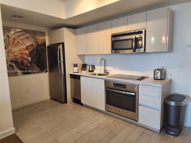 kitchen with appliances with stainless steel finishes, white cabinets, light hardwood / wood-style flooring, and sink