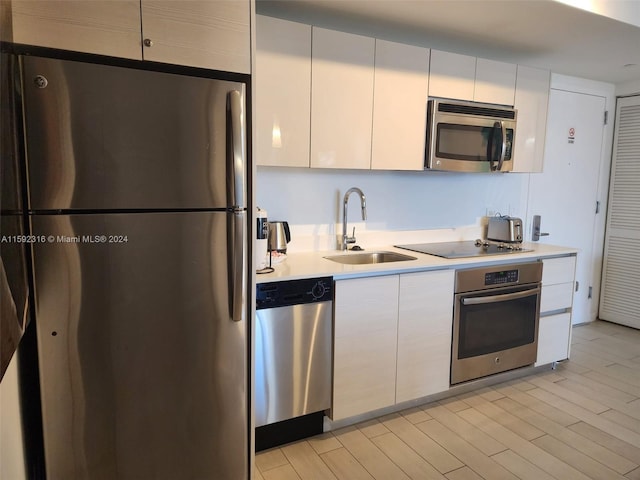 kitchen with white cabinets, appliances with stainless steel finishes, sink, and light wood-type flooring