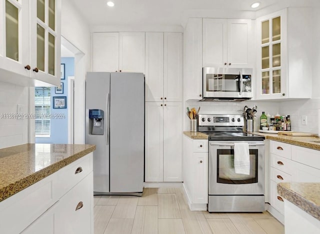 kitchen featuring backsplash, appliances with stainless steel finishes, light stone countertops, and white cabinetry