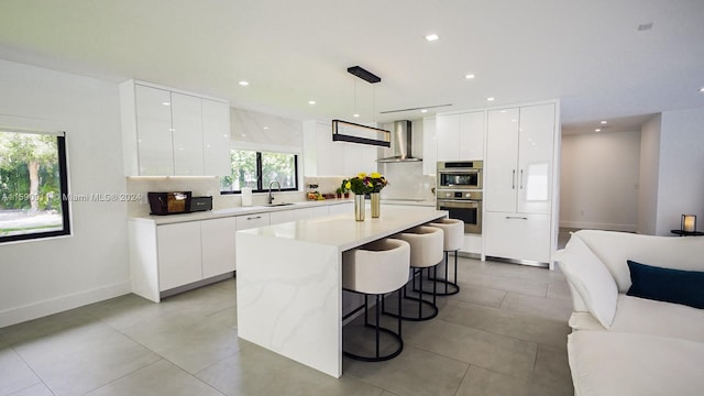 kitchen with wall chimney range hood, white cabinetry, pendant lighting, and a center island