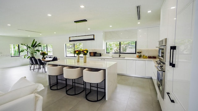 kitchen with white cabinets, hanging light fixtures, sink, and a kitchen island