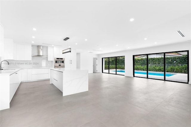 kitchen with white cabinetry, sink, a kitchen island, wall chimney range hood, and pendant lighting