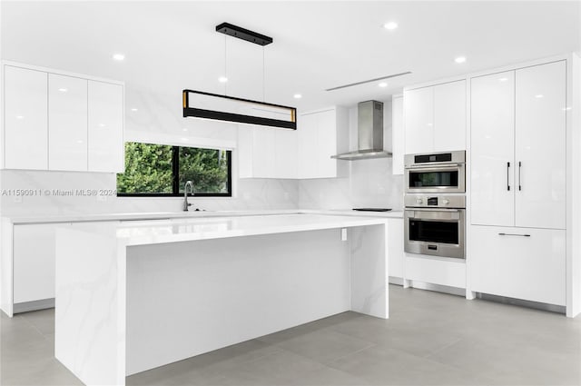 kitchen with white cabinets, wall chimney exhaust hood, decorative light fixtures, and double oven