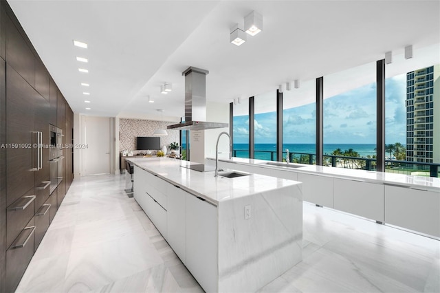 kitchen with white cabinets, decorative backsplash, island range hood, light tile patterned floors, and a kitchen island with sink