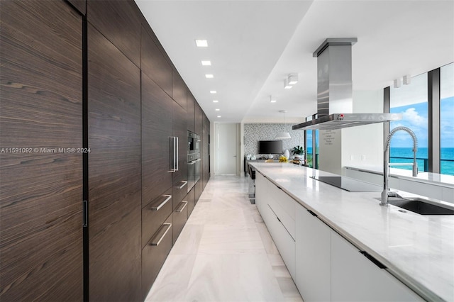 kitchen with black electric cooktop, light tile patterned floors, dark brown cabinetry, island range hood, and sink