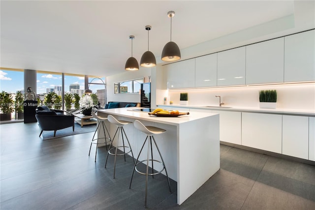 kitchen with a center island, white cabinetry, decorative light fixtures, a wall of windows, and sink