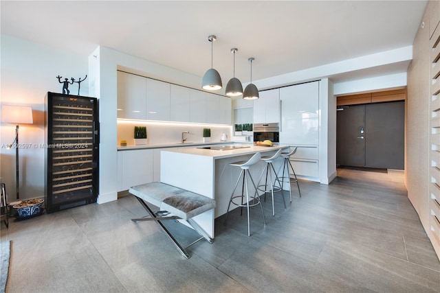 kitchen featuring decorative light fixtures, stainless steel oven, white cabinetry, and a breakfast bar