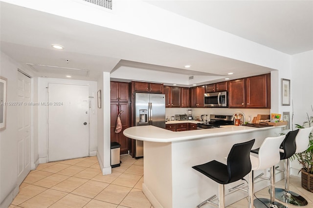 kitchen with appliances with stainless steel finishes, a breakfast bar area, light tile flooring, and kitchen peninsula