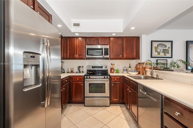 kitchen with appliances with stainless steel finishes, a tray ceiling, sink, and light tile floors