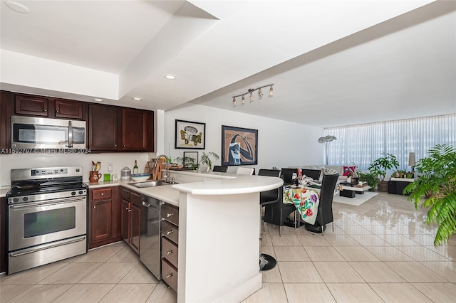 kitchen featuring stainless steel appliances, sink, light tile floors, and kitchen peninsula