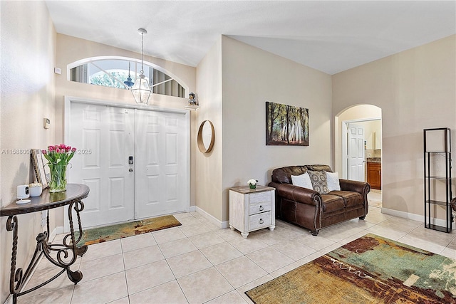 foyer featuring light tile patterned floors, an inviting chandelier, arched walkways, and baseboards