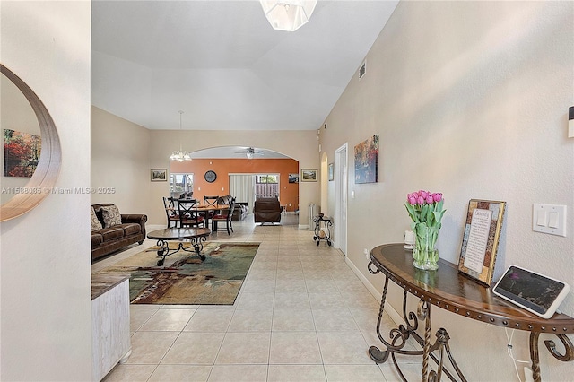 living area with arched walkways, light tile patterned floors, ceiling fan with notable chandelier, baseboards, and vaulted ceiling