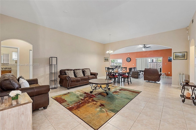 living area with arched walkways, light tile patterned floors, ceiling fan with notable chandelier, and baseboards