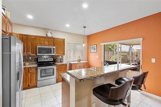 kitchen featuring a breakfast bar, pendant lighting, backsplash, appliances with stainless steel finishes, and brown cabinetry