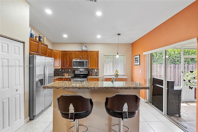 kitchen featuring a breakfast bar, a kitchen island, hanging light fixtures, appliances with stainless steel finishes, and brown cabinetry