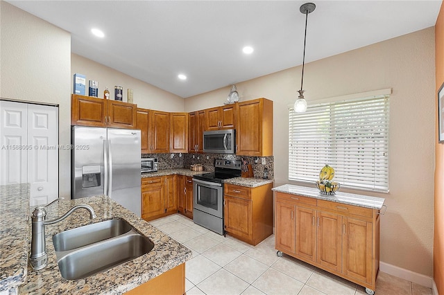 kitchen with a sink, appliances with stainless steel finishes, backsplash, brown cabinets, and decorative light fixtures