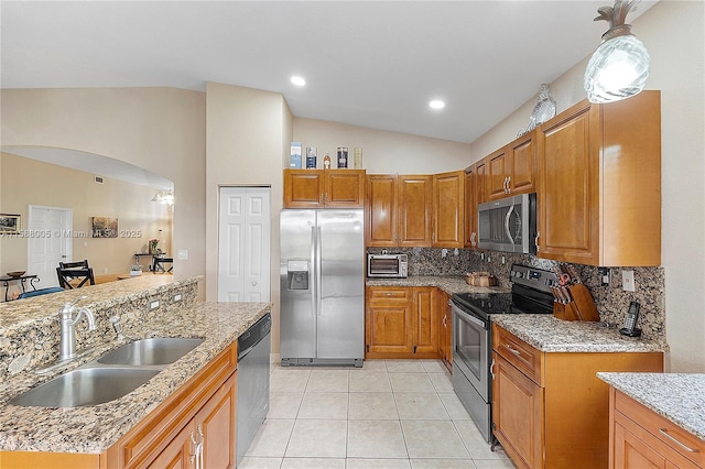 kitchen featuring arched walkways, light stone counters, stainless steel appliances, a sink, and vaulted ceiling