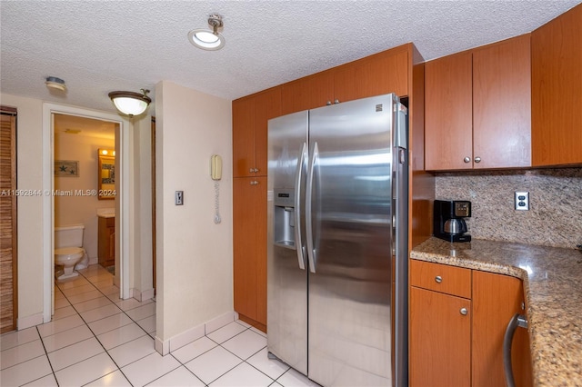 kitchen featuring a textured ceiling, backsplash, light tile flooring, and stainless steel refrigerator with ice dispenser