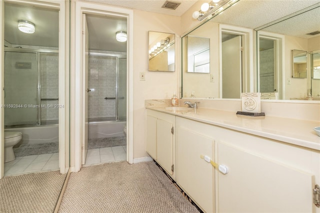 full bathroom with a textured ceiling, tile floors, combined bath / shower with glass door, vanity, and toilet