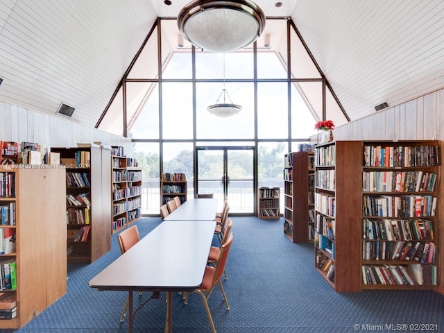 interior space featuring expansive windows, high vaulted ceiling, wooden walls, and carpet flooring