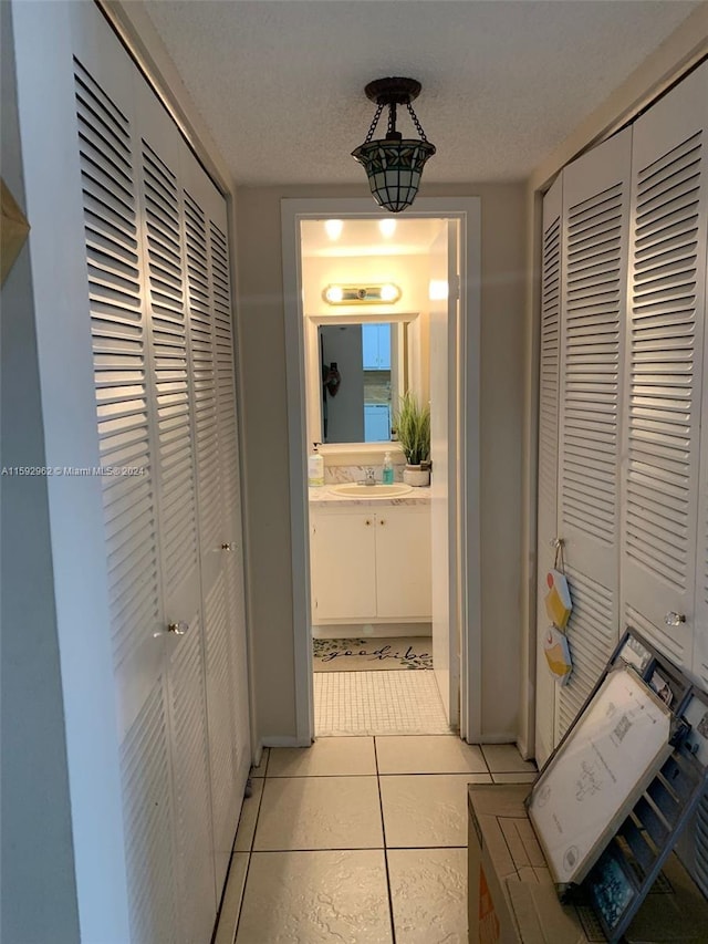 corridor featuring sink, a textured ceiling, and light tile floors