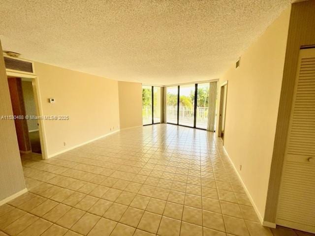 unfurnished room featuring a textured ceiling, a wall of windows, visible vents, and baseboards