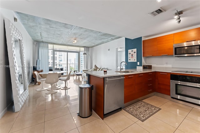 kitchen featuring stainless steel appliances, kitchen peninsula, a wall of windows, sink, and light tile flooring