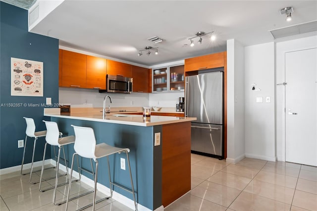 kitchen featuring kitchen peninsula, track lighting, appliances with stainless steel finishes, sink, and light tile floors