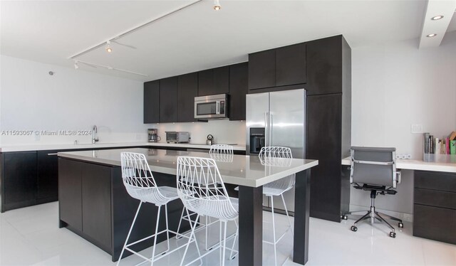 kitchen with light tile floors, rail lighting, a center island, a kitchen bar, and appliances with stainless steel finishes