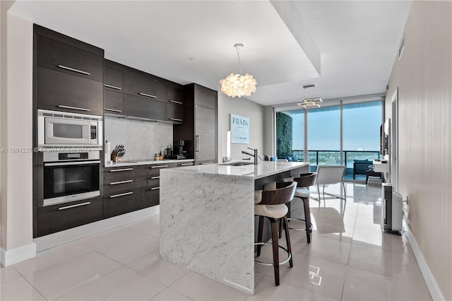 kitchen featuring a kitchen breakfast bar, stainless steel appliances, a center island with sink, pendant lighting, and backsplash