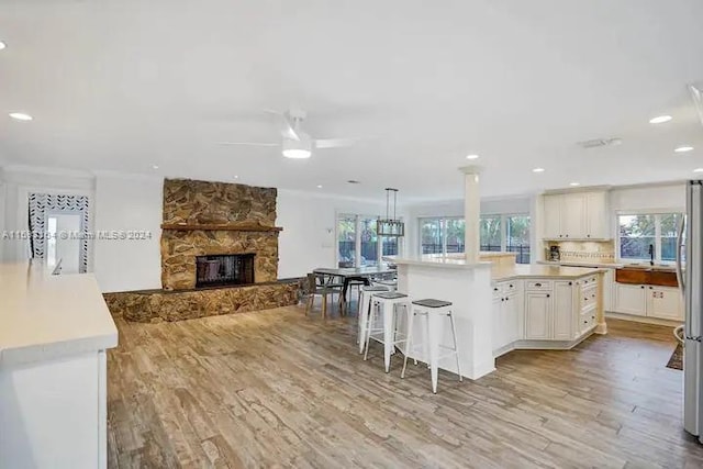 kitchen featuring a stone fireplace, ceiling fan, light wood-type flooring, pendant lighting, and a center island