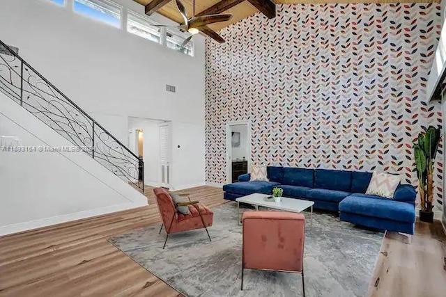 living room with a towering ceiling, beamed ceiling, hardwood / wood-style floors, and ceiling fan