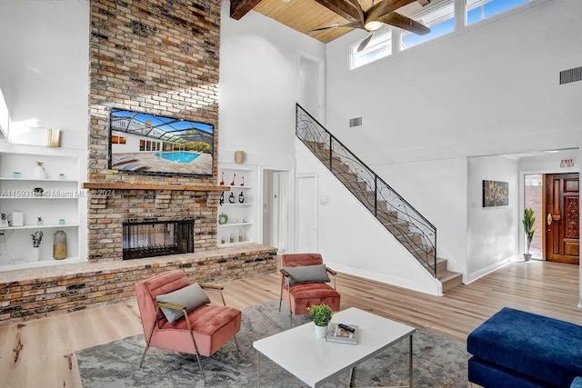 living room with a brick fireplace, a towering ceiling, ceiling fan, wood-type flooring, and built in shelves