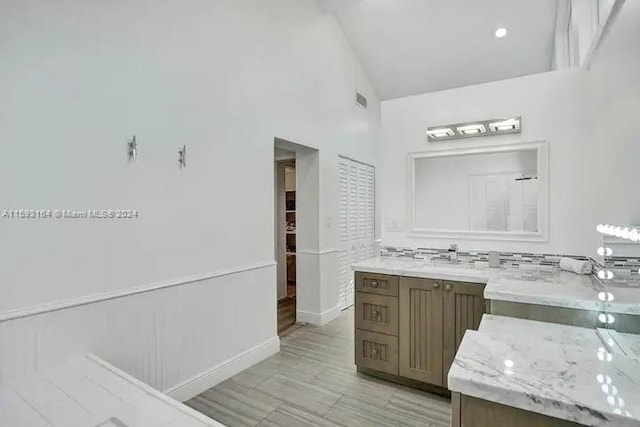 bathroom featuring high vaulted ceiling, oversized vanity, and tasteful backsplash