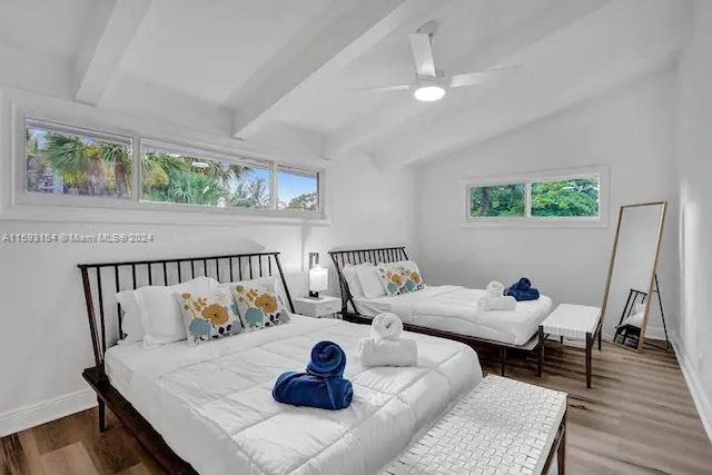 bedroom with ceiling fan, multiple windows, hardwood / wood-style floors, and vaulted ceiling with beams