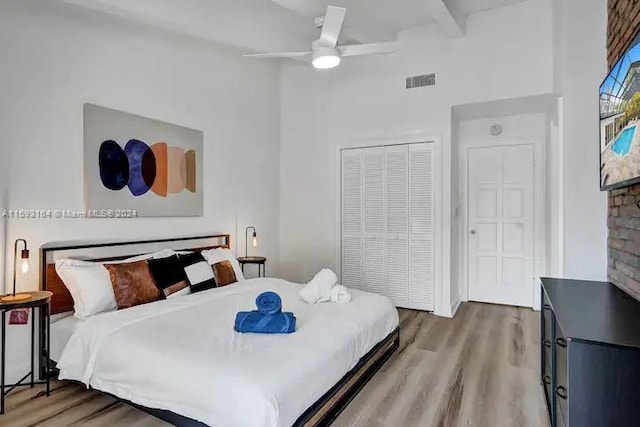 bedroom featuring ceiling fan, a closet, beam ceiling, wood-type flooring, and a towering ceiling