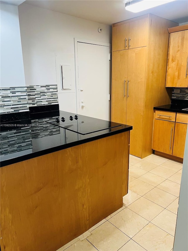 kitchen with dark stone countertops, light tile patterned floors, kitchen peninsula, and decorative backsplash