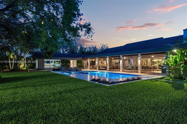 pool at dusk featuring a patio and a lawn