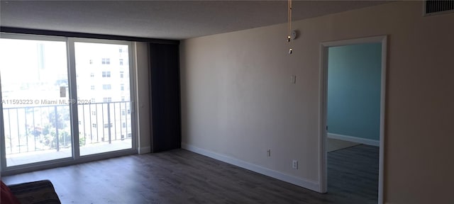 empty room with dark wood-type flooring, a textured ceiling, and a wall of windows