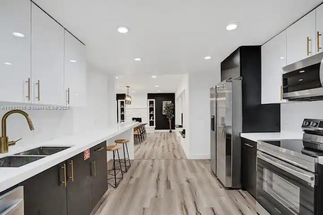 kitchen with sink, a breakfast bar area, light wood-type flooring, stainless steel appliances, and white cabinets