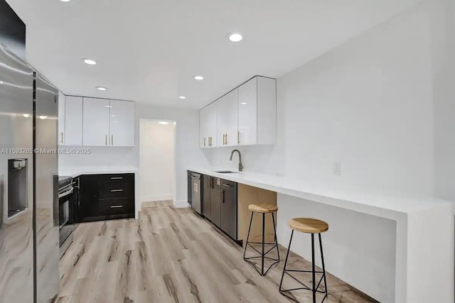 kitchen featuring a breakfast bar, sink, stainless steel fridge, white cabinets, and light hardwood / wood-style floors