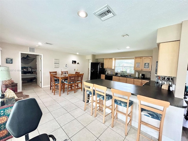 kitchen featuring black fridge, a textured ceiling, kitchen peninsula, light tile floors, and light brown cabinets