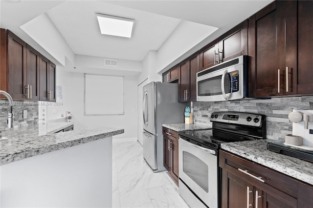 kitchen with dark brown cabinetry, light tile flooring, stainless steel appliances, tasteful backsplash, and light stone countertops