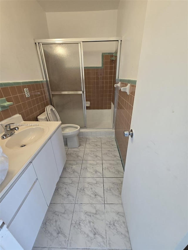 bathroom with a shower with shower door, vanity, toilet, and tile walls