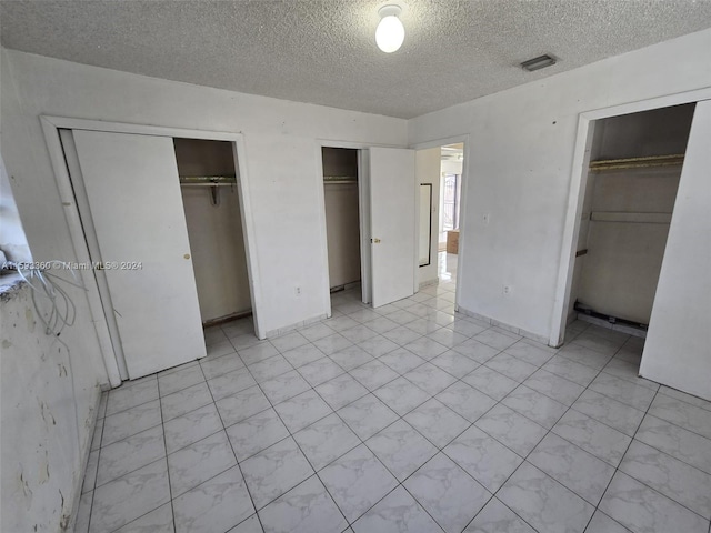 unfurnished bedroom featuring multiple closets and a textured ceiling