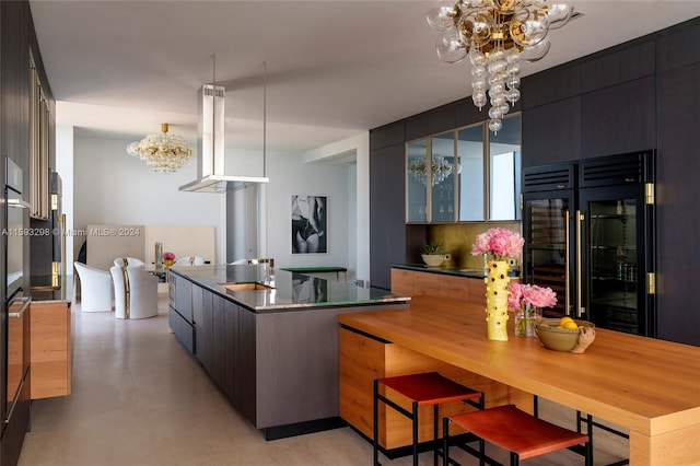 kitchen featuring decorative light fixtures, wall chimney range hood, a chandelier, a breakfast bar, and built in refrigerator