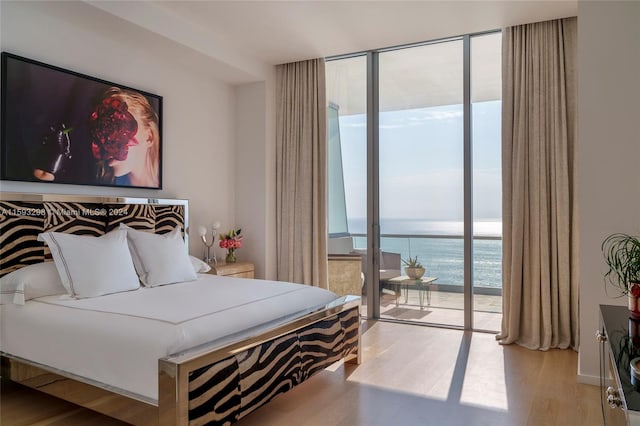 bedroom featuring a water view, floor to ceiling windows, light wood-type flooring, and access to outside