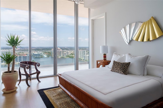 bedroom featuring access to exterior, a wall of windows, hardwood / wood-style flooring, and a water view