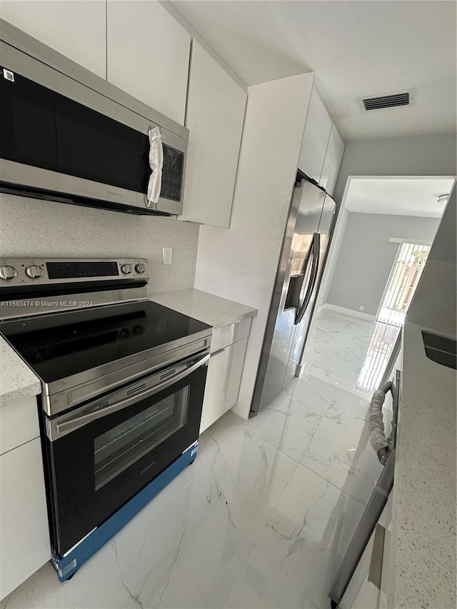 kitchen with tasteful backsplash, stainless steel appliances, light stone countertops, light tile patterned flooring, and white cabinetry